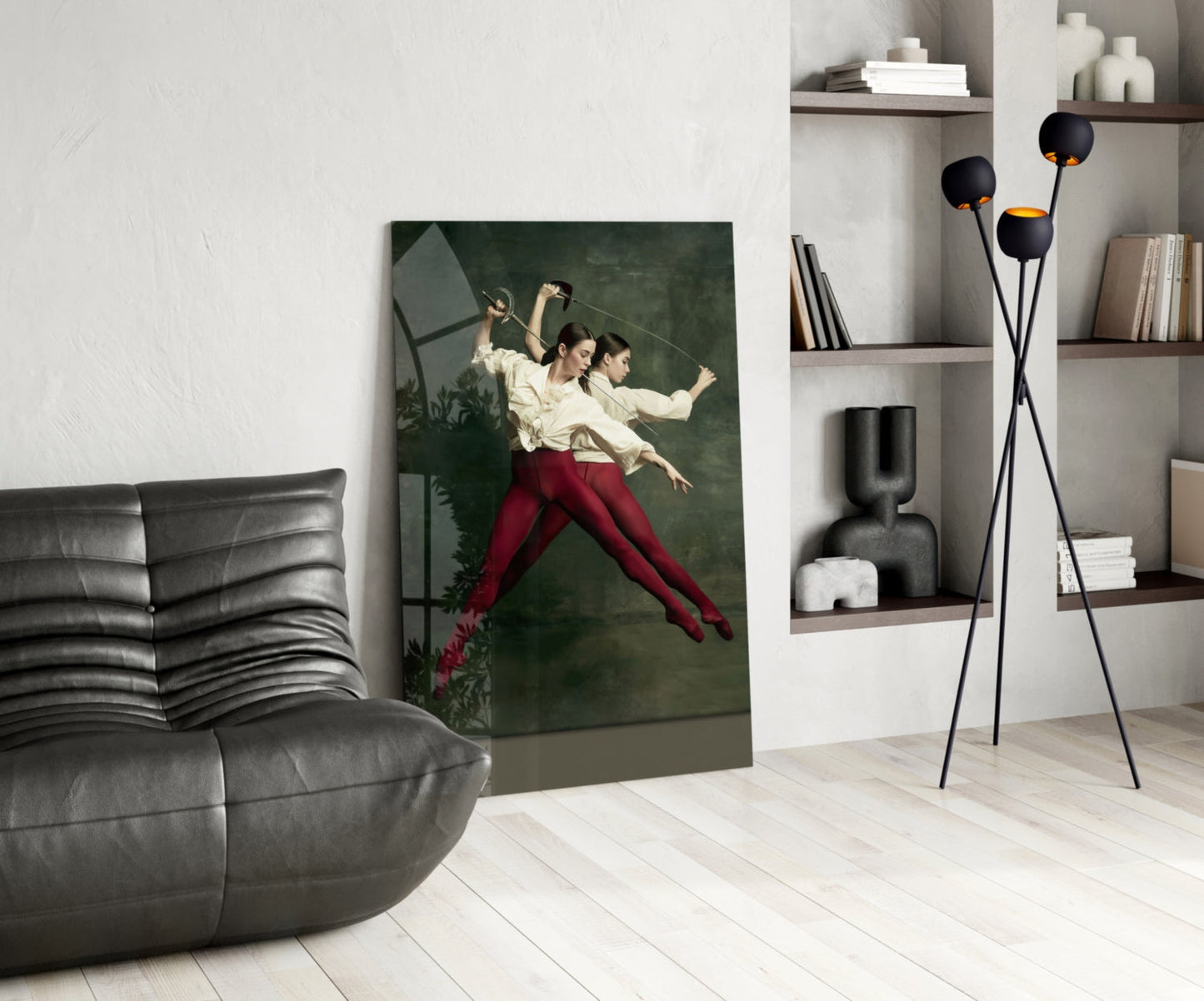 Glass wall art depicting two ballet dancers in cream shirts and red pants leaning against dark green background, displayed in modern living room setting.