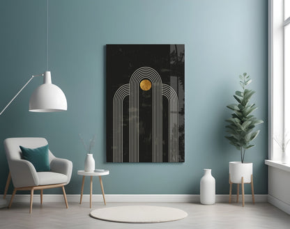 Modern living room scene with black glass wall art displaying white concentric arches and gold circle, mounted above cream chair.