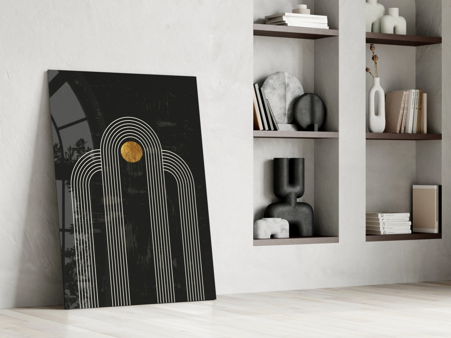 Black glass wall art with white concentric arches and gold circle leaning against white wall beside wooden shelving unit.
