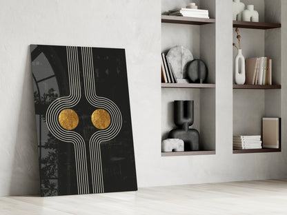 Modern minimalist interior with leaning abstract black glass art featuring white geometric lines and gold circular accents, beside white wall shelving displaying books and decorative objects.