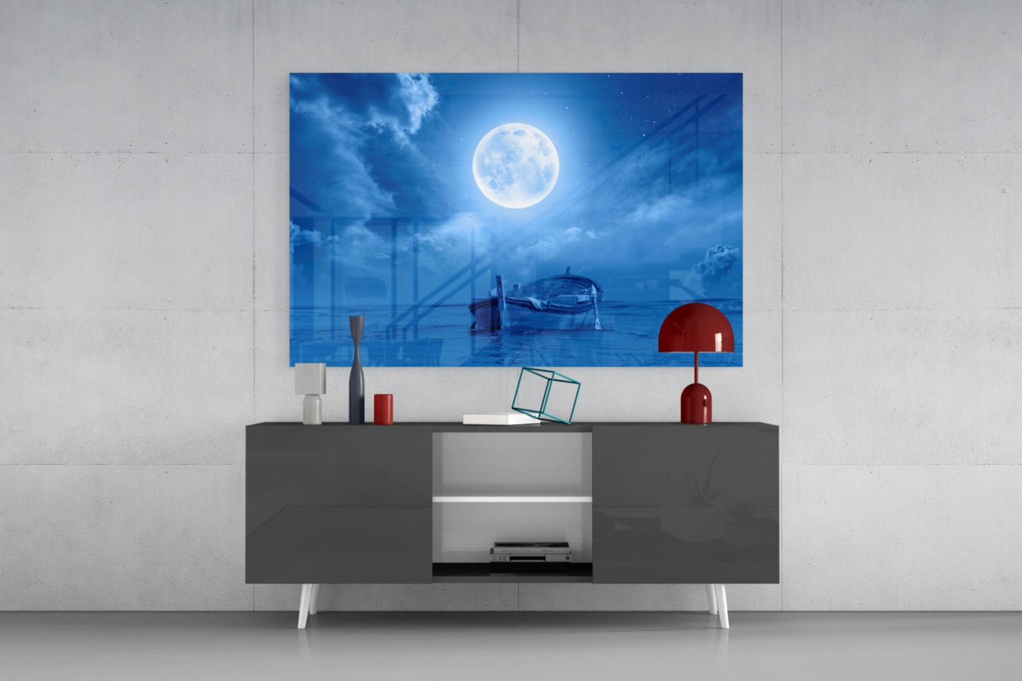 Glass wall art depicting a full moon over a moonlit ocean with boats, displayed above a dark gray media console with red decorative lamp.