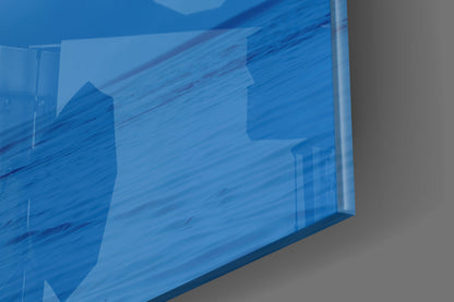 Close-up angled view of blue translucent glass wall art showing layered architectural silhouettes and water textures.