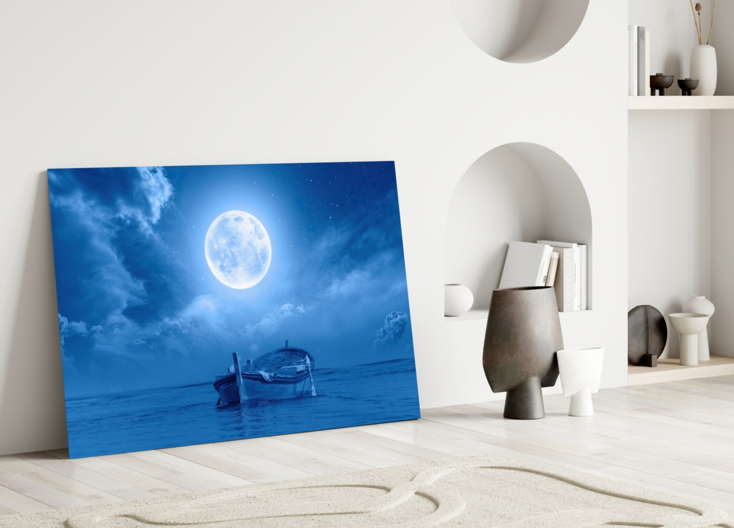 Blue glass wall art depicting a full moon over water with a boat, displayed in a minimalist white room with shelving.