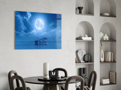 Glass wall art depicting a moonlit ocean scene with a wooden boat, displayed above a round black dining table in a modern interior.