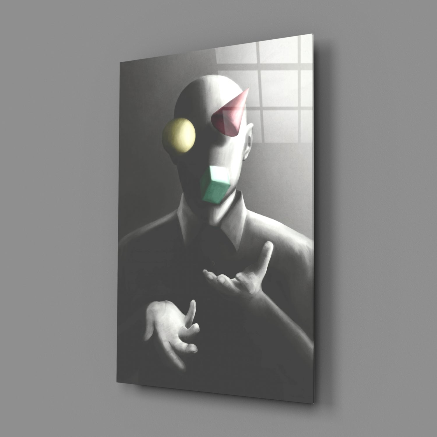 Angled view of glass wall art showing monochromatic sculptural figure with colored geometric shapes on face against gridded window background.