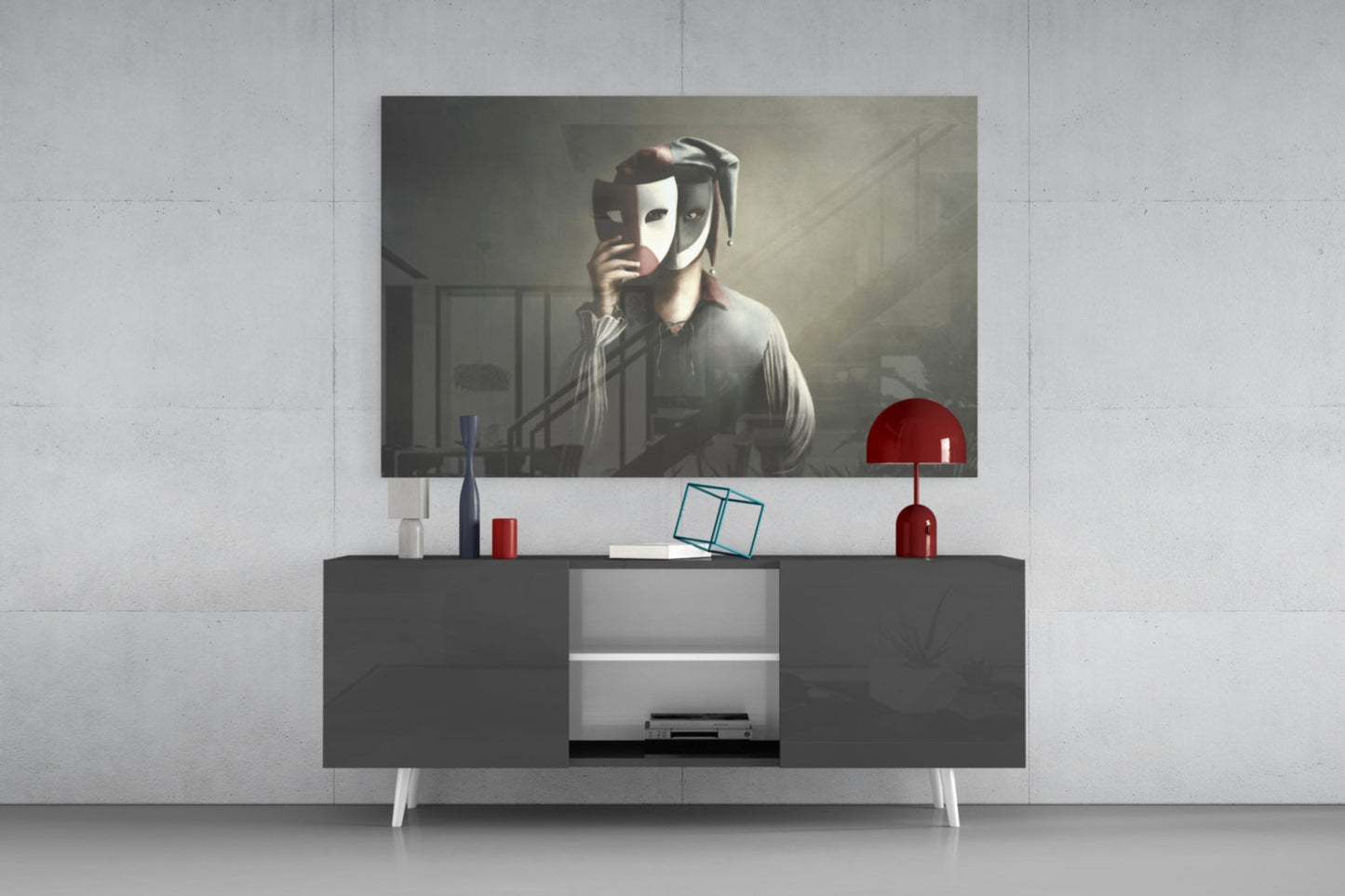 Glass wall art featuring dramatic figure holding theatrical masks displayed above modern dark sideboard with red lamp and accessories.