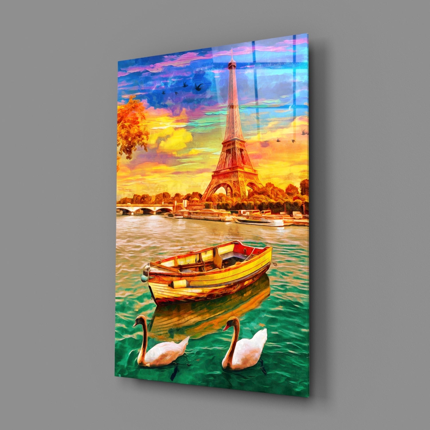 Glass wall art panel displaying an Eiffel Tower sunset scene with a yellow boat and white swans in the foreground water.