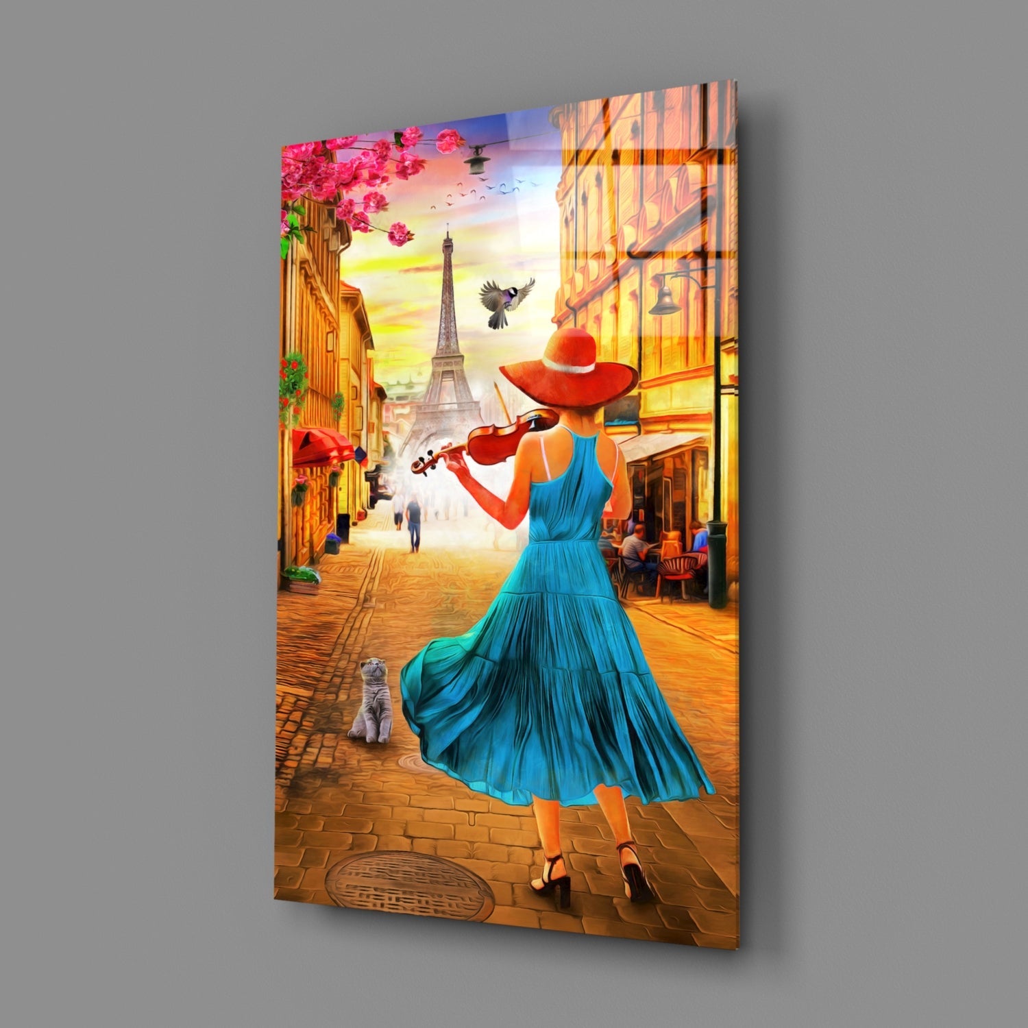 Glass wall art panel displayed at an angle showing a woman in blue dress playing violin on a Parisian street at sunset.