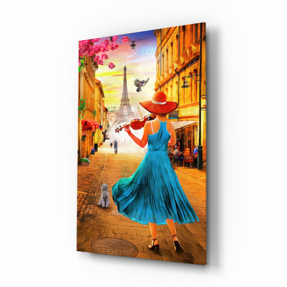 Glass wall art panel showing angled 3D perspective of woman in blue dress playing violin on Paris street with Eiffel Tower at sunset.