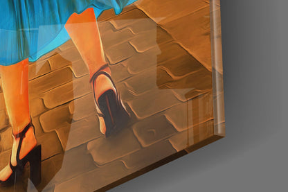 Close-up angled view of glass wall art featuring orange and black brushstroke design on textured brown brick background with blue sky element.