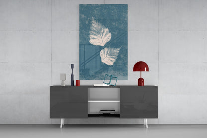 Teal glass wall art with white leaf designs displayed above a dark media console with red and white decorative accessories.