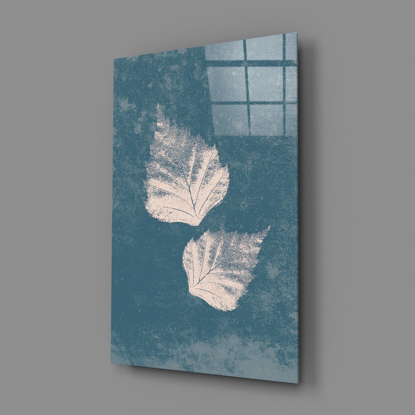 Angled view of teal glass wall art with two white leaf impressions and window pane reflection shadow.