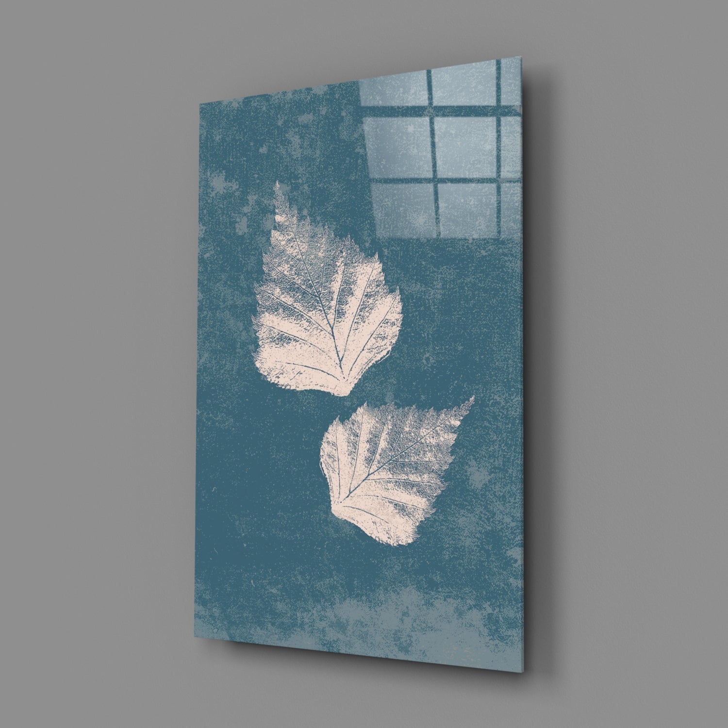 Angled view of teal glass wall art with two white leaf impressions and window pane reflection shadow.