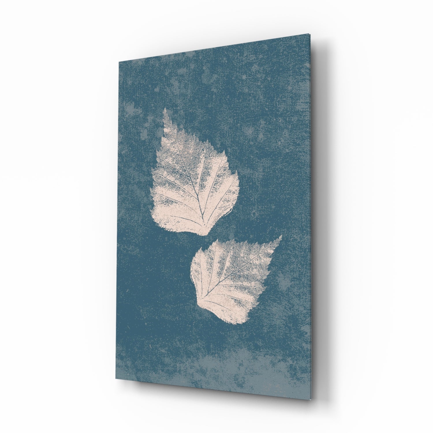 Angled view of glass wall art featuring two white leaf imprints on textured teal background with shadow effect.