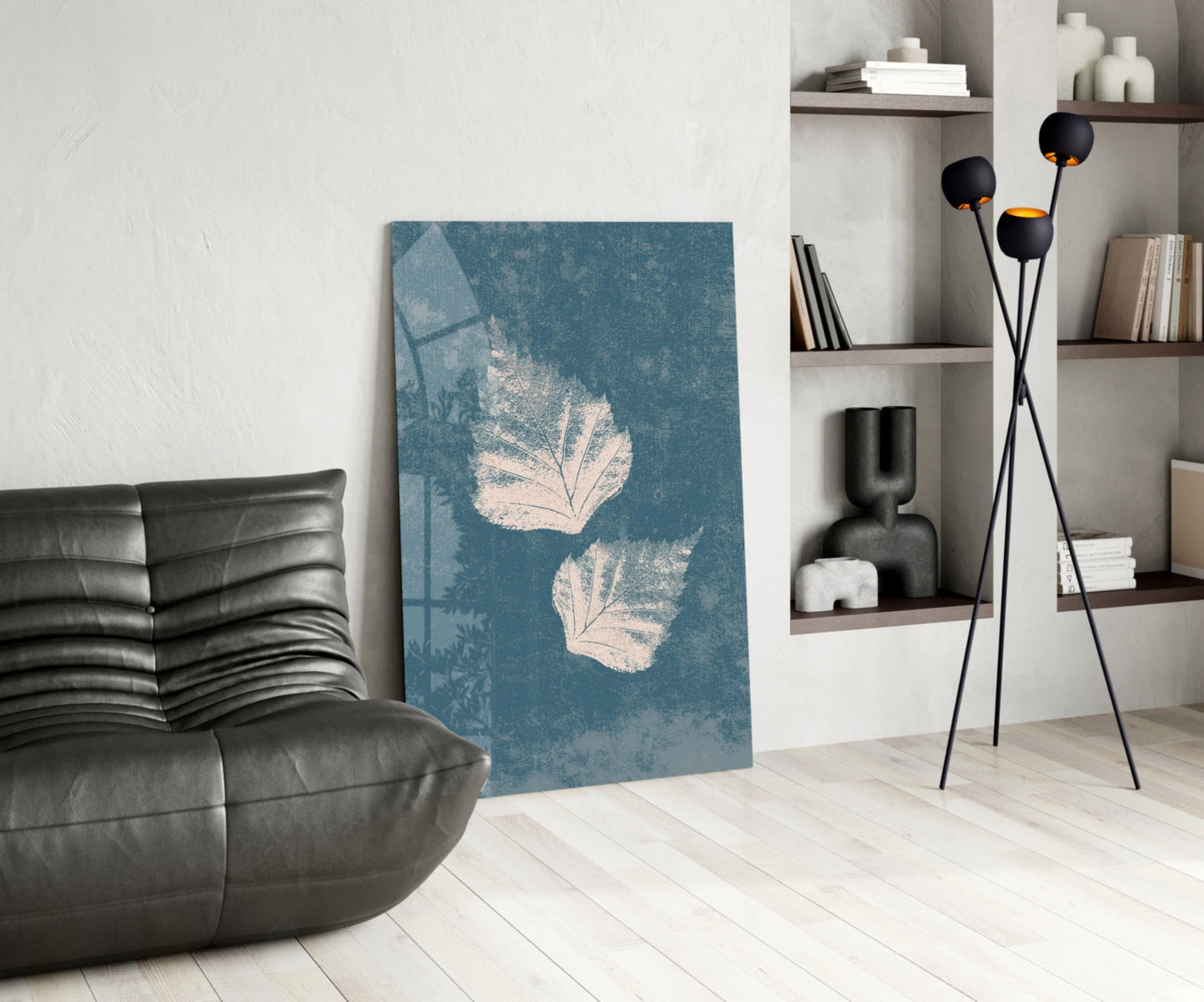 Teal glass wall art with white leaf prints displayed in modern living room next to black leather chair and floor lamp.