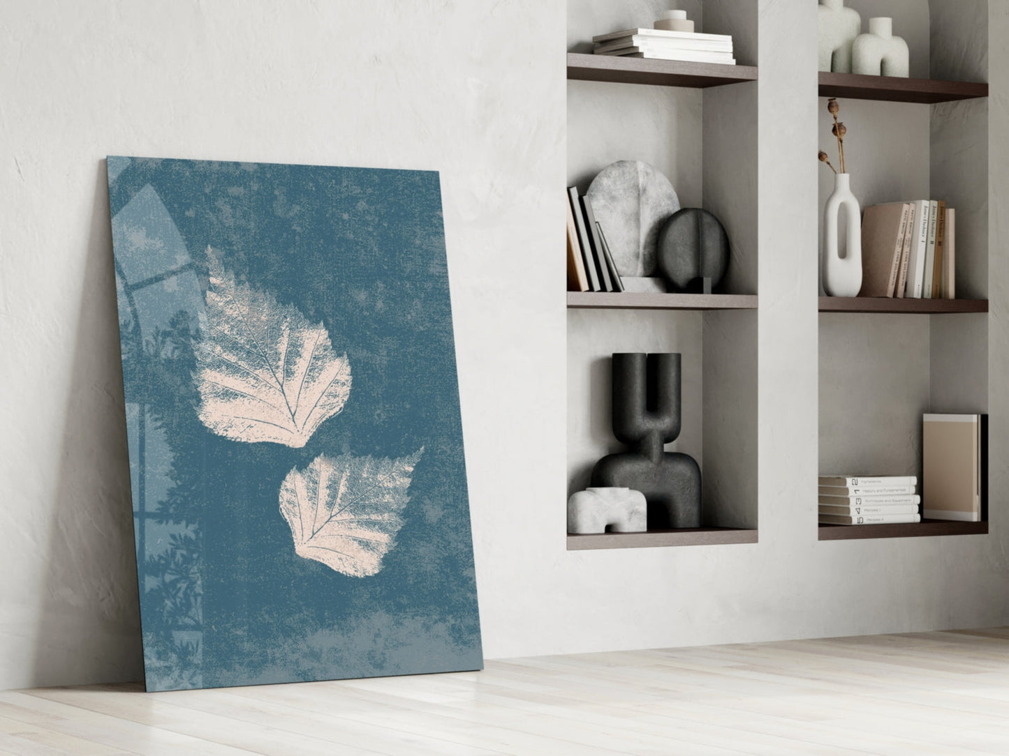 Blue glass wall art with cream leaf prints leaning against white wall beside shelving unit.