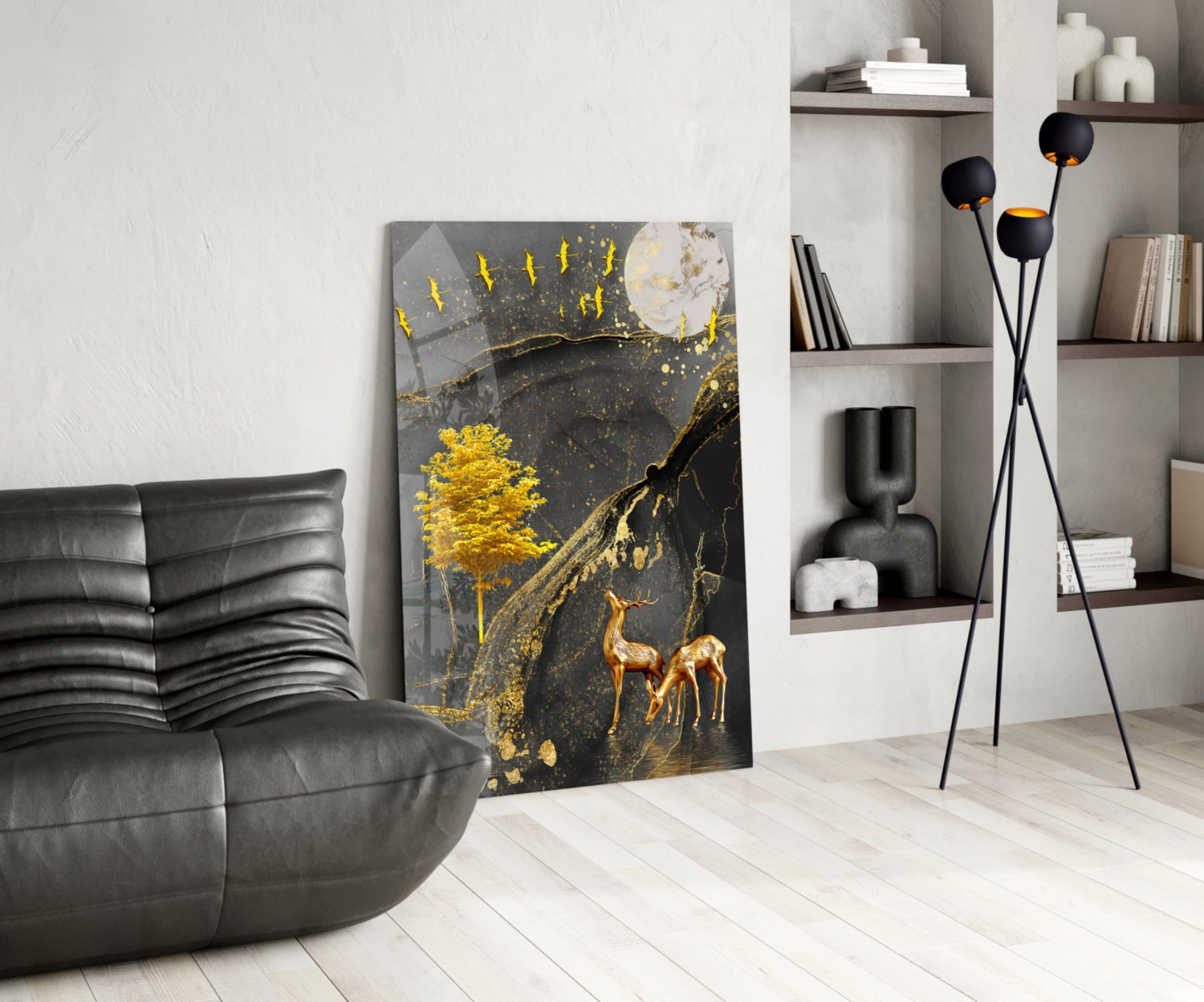 Modern living room with black leather sofa, gold and black tree artwork leaning against wall, tripod floor lamp, and white shelving unit.