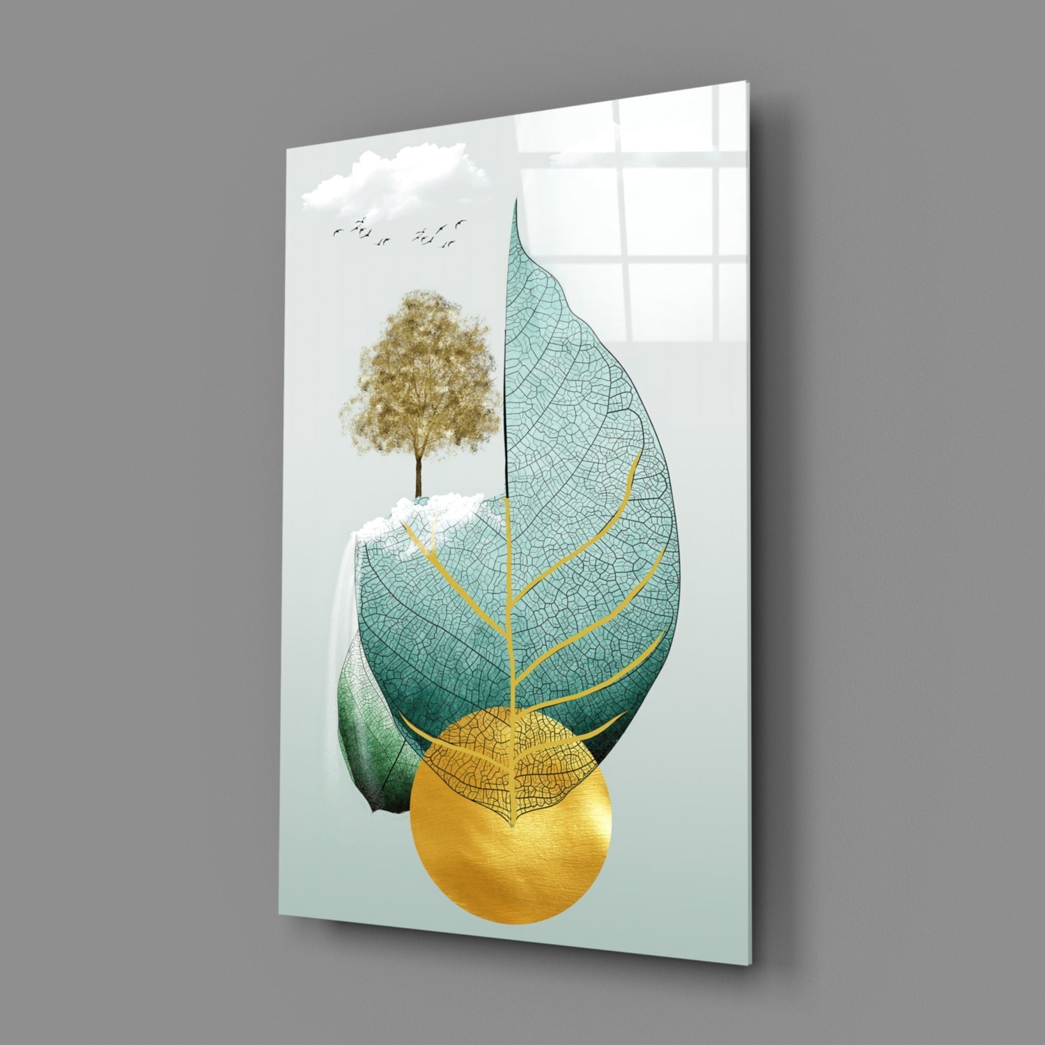 Glass wall art displaying a composite botanical illustration with a golden tree, layered leaves in teal and green with gold veining, and a yellow circle, angled three-quarter view against gray background.