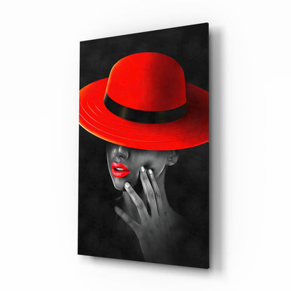 Glass wall art panel displaying a woman in profile wearing a dramatic red wide-brimmed hat with black band against dark background.