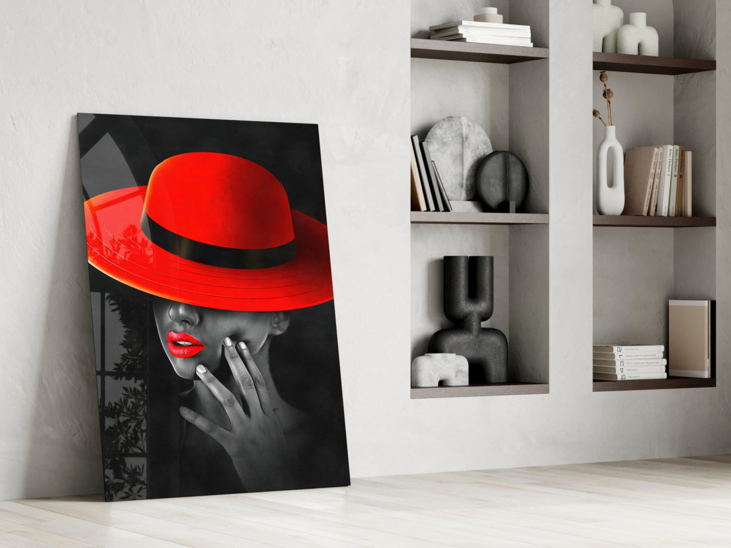 Modern interior room display featuring a leaning glass art print of a woman in a red hat against black and white background, beside white shelving with decorative objects and books.