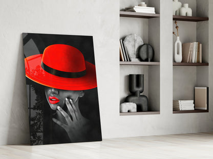 Modern interior room display featuring a leaning glass art print of a woman in a red hat against black and white background, beside white shelving with decorative objects and books.