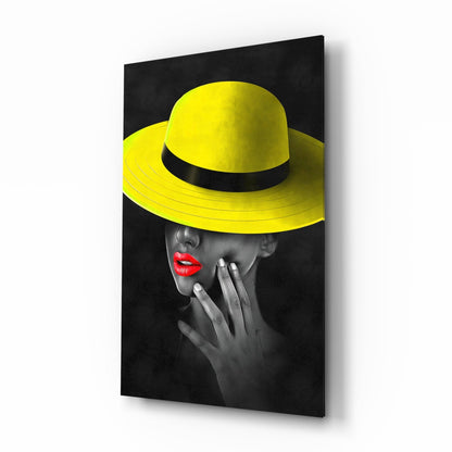 Glass wall art displaying a grayscale portrait with bright yellow wide-brimmed hat and red lips against black background, angled view showing 3D depth.