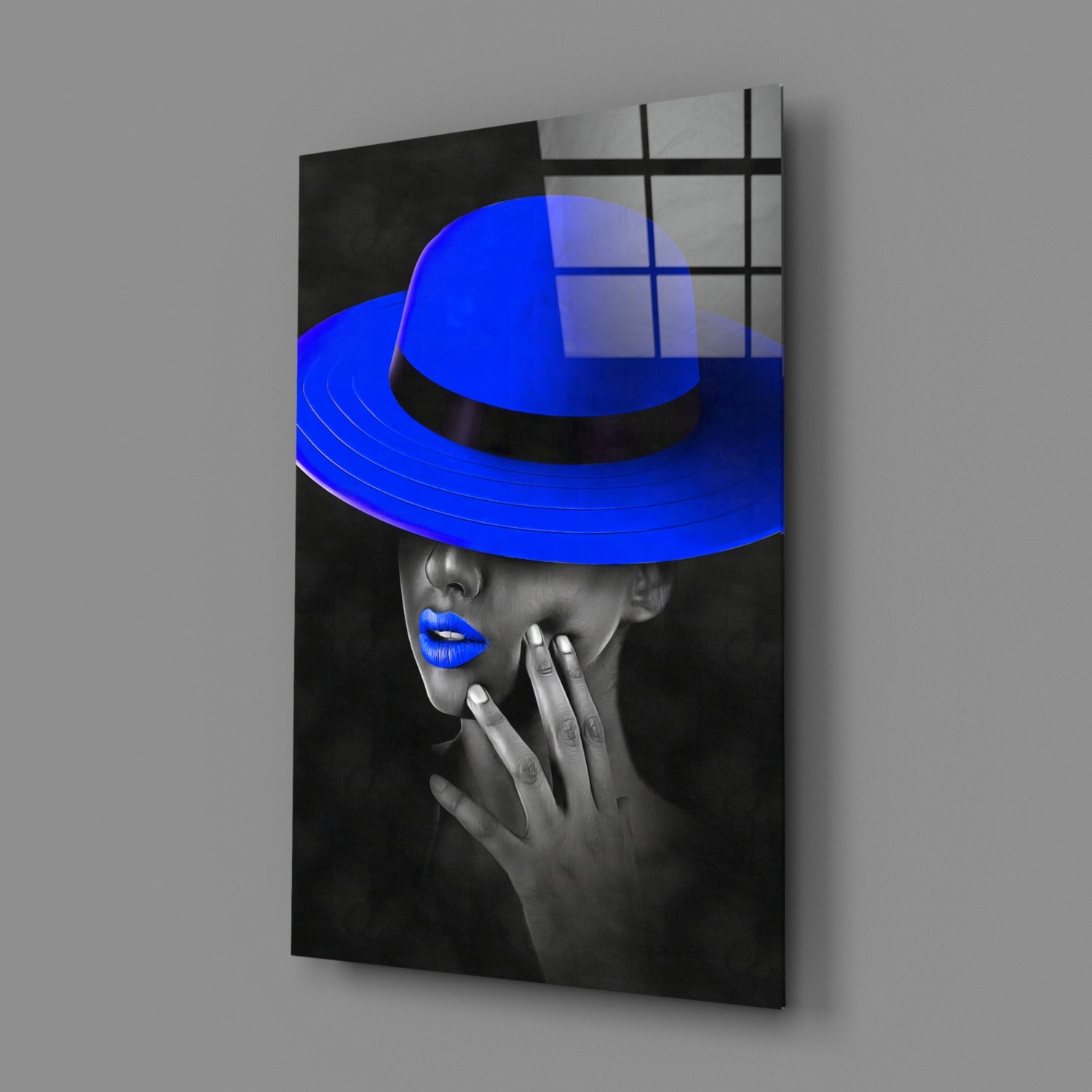 Angled view of glass wall art featuring black-and-white portrait with vibrant blue hat and lips, mounted on gray wall.