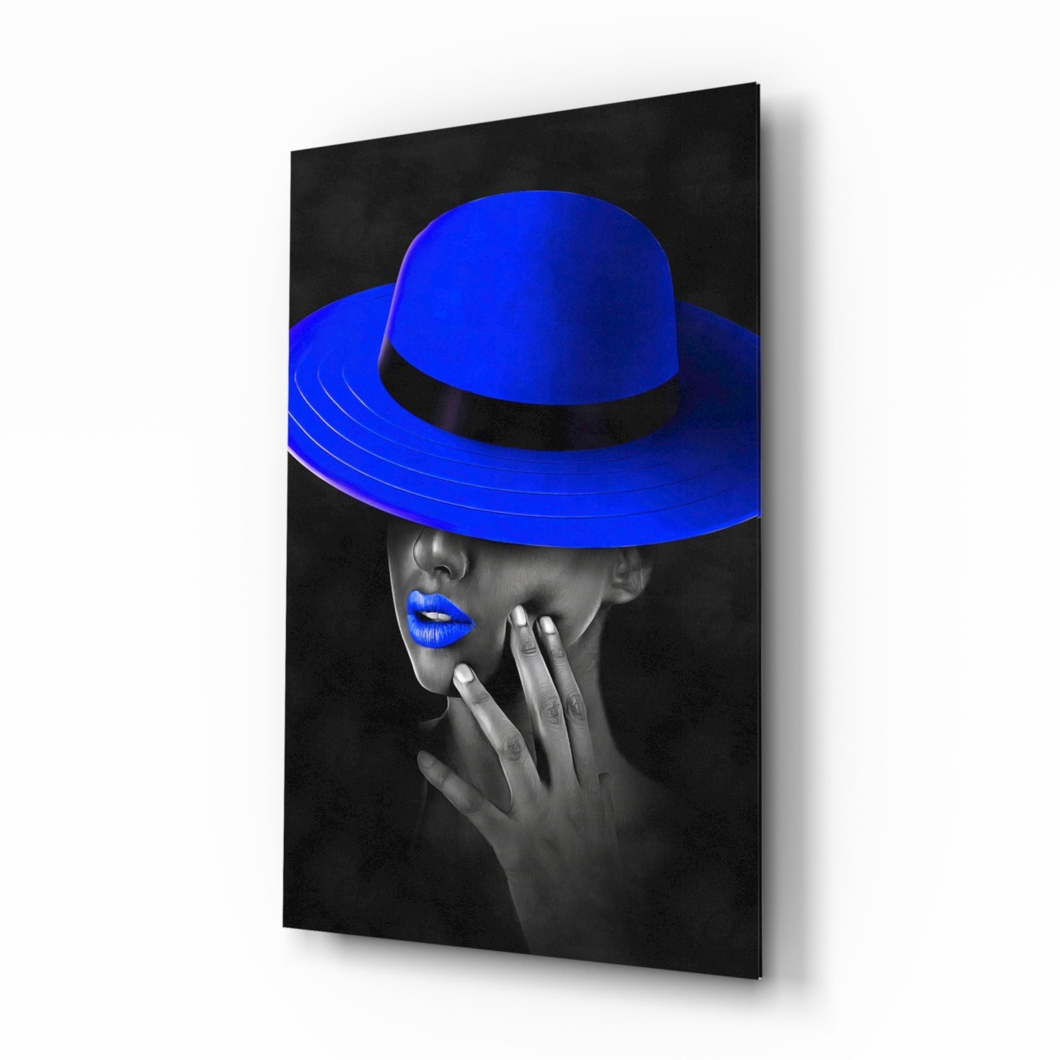 Three-quarter angle view of glass wall art featuring monochrome portrait with vibrant blue wide-brimmed hat and lips against black background.