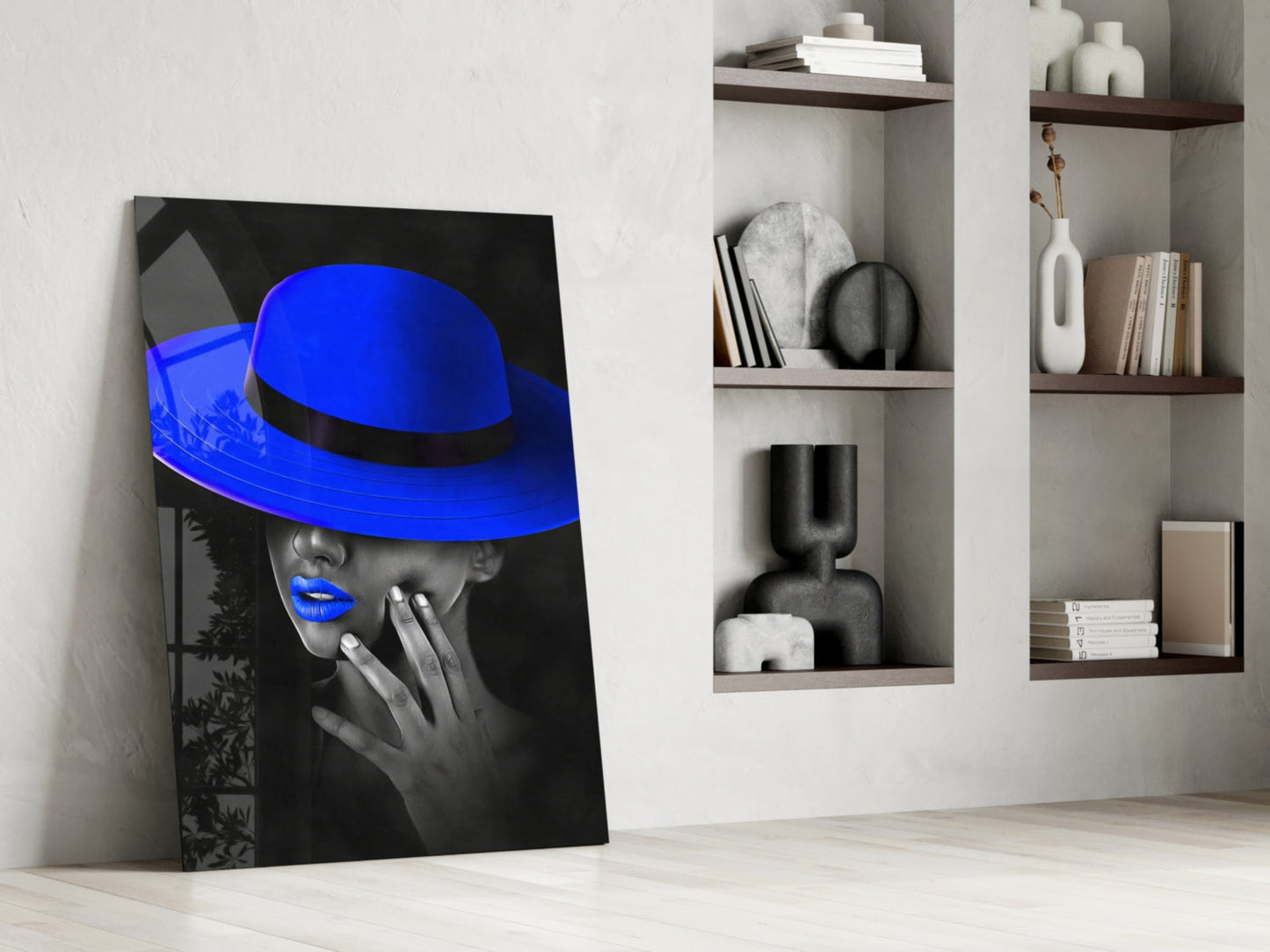 Blue Hat Glass Wall Art leaning against white wall next to shelving unit displaying decorative objects and books.