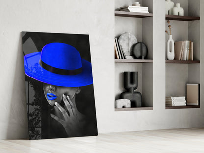 Blue Hat Glass Wall Art leaning against white wall next to shelving unit displaying decorative objects and books.
