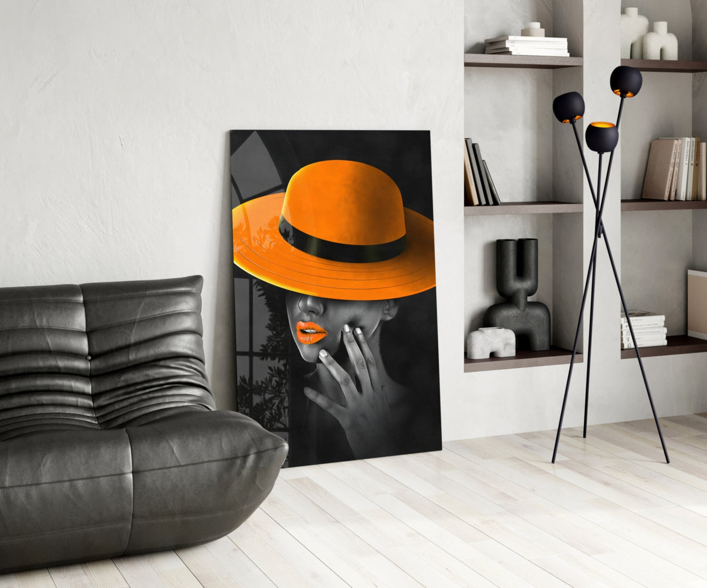 Orange hat glass wall art leaning against wall in modern living room with gray sofa and shelving.