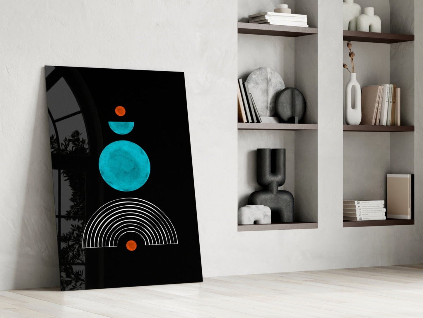 Modern minimalist glass wall art leaning against white wall beside built-in shelving, featuring turquoise circles, orange dots, and white arc lines on black background.