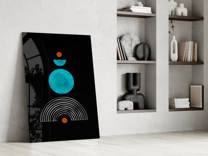 Modern minimalist glass wall art leaning against white wall beside built-in shelving, featuring turquoise circles, orange dots, and white arc lines on black background.