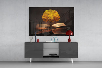 Glass wall art depicting a golden tree growing from open books displayed on a dark media console with red decorative accessories.