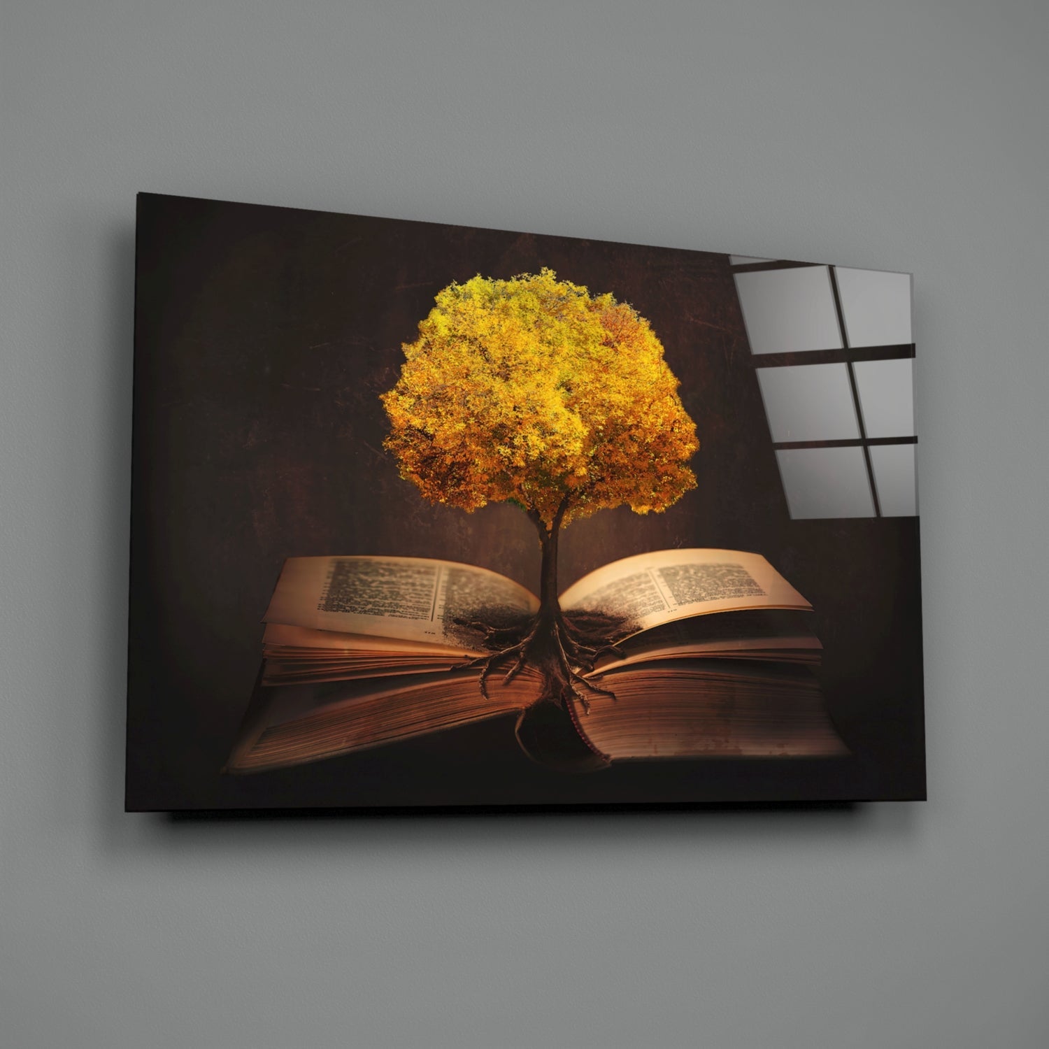 Glass wall art displaying a golden tree with roots growing from an open book against a dark brown background, angled view showing glass panels on right side.