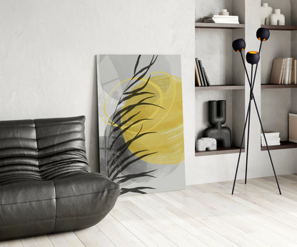 Modern living room with yellow and black botanical glass wall art leaning against white wall beside black leather chair.