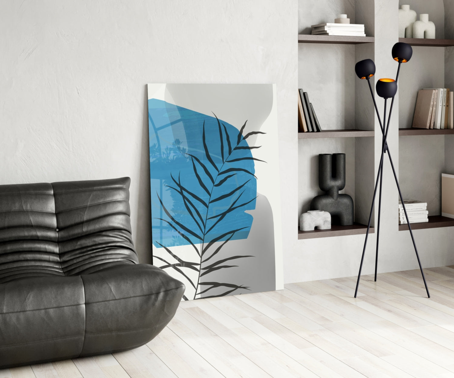 Modern living room with blue and black leaf glass wall art displayed next to black leather chair and shelving unit.