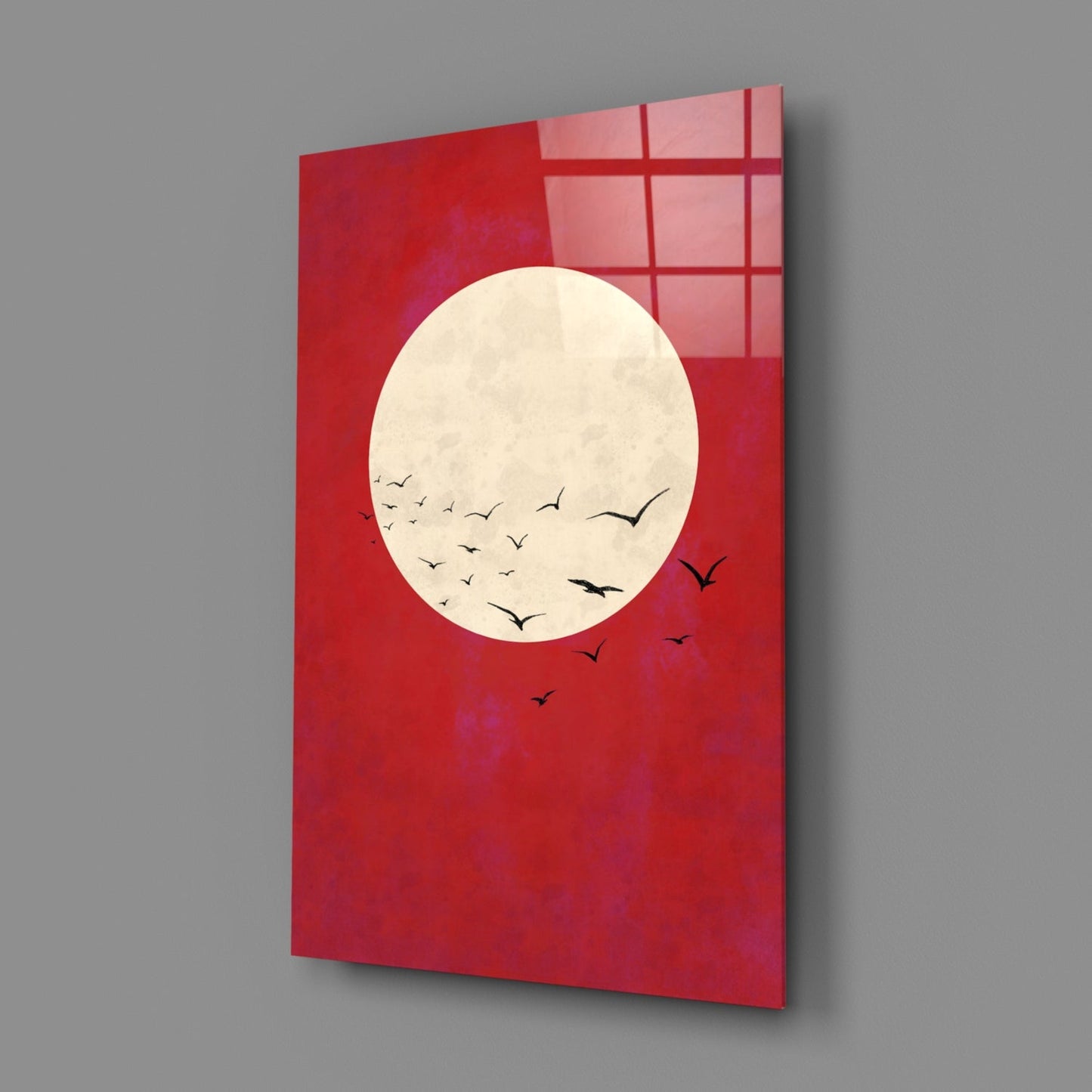 Red glass wall art panel displaying a cream moon with flying birds, viewed at an angle against gray background.