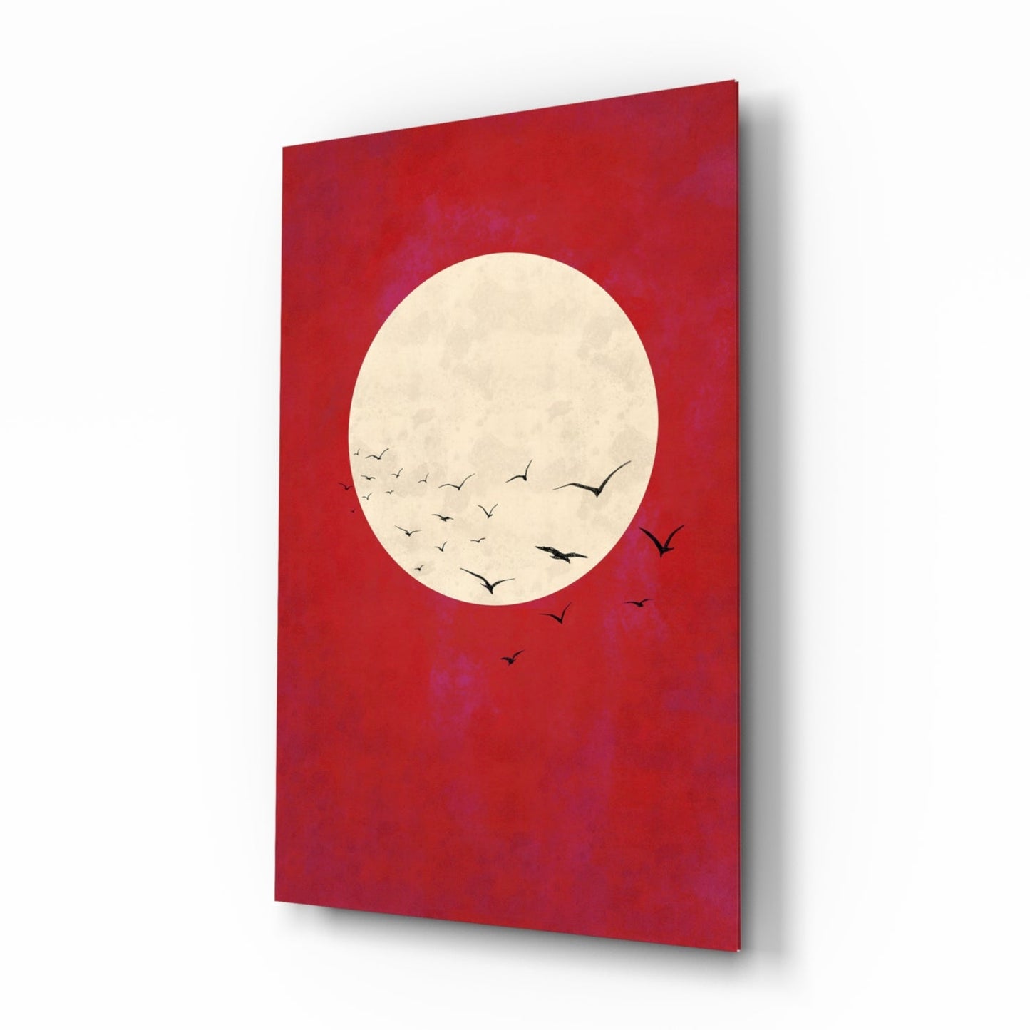 Red glass wall art panel displayed at an angle, featuring a cream moon with silhouetted birds in flight against deep red background.