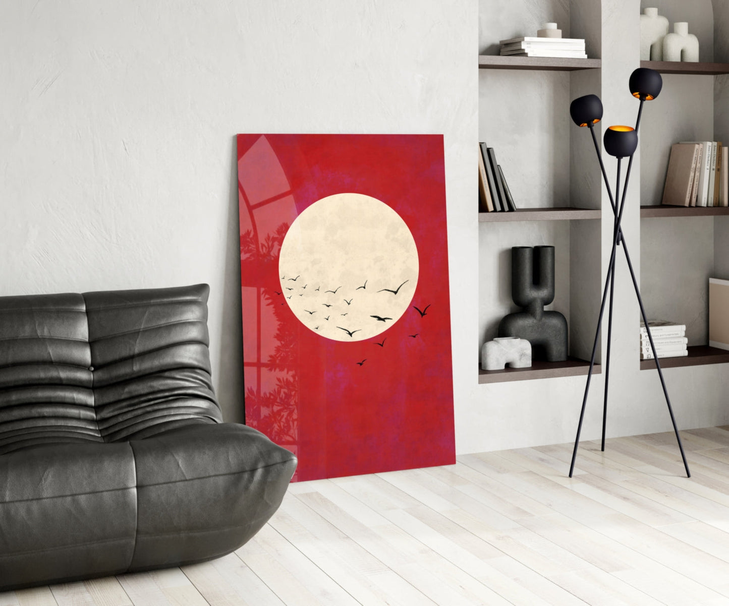 Red glass wall art featuring cream moon with black flying birds, displayed in modern living room with black leather chair and shelving.
