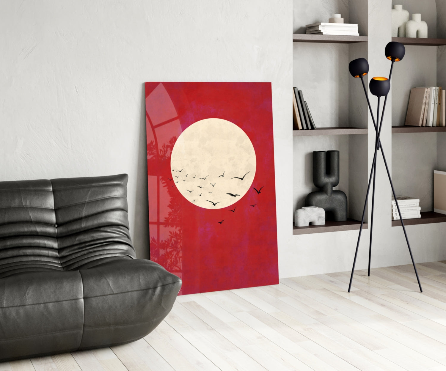 Red glass wall art featuring cream moon with black flying birds, displayed in modern living room with black leather chair and shelving.