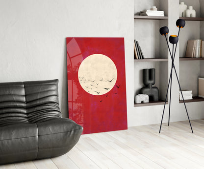 Red glass wall art featuring cream moon with black flying birds, displayed in modern living room with black leather chair and shelving.