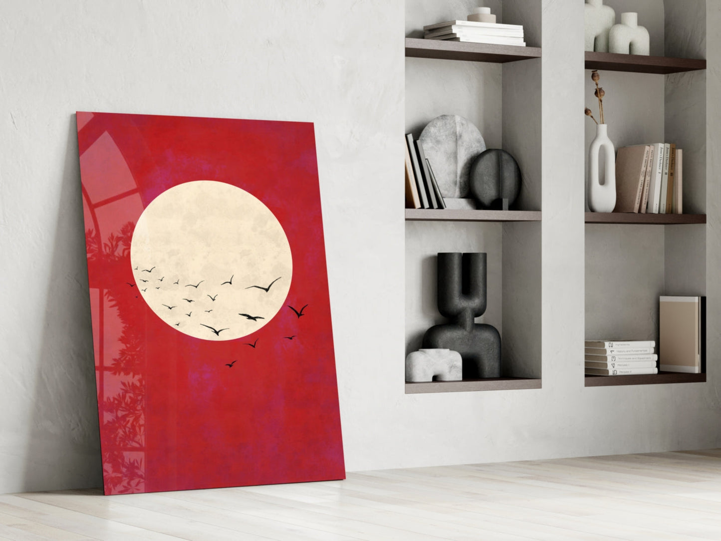 Red glass wall art leaning against white wall beside white shelving unit displaying decorative objects and books.