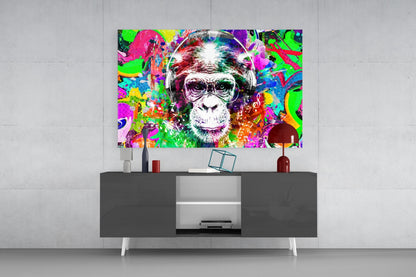 Vibrant pop art glass wall art depicting a chimpanzee wearing headphones, displayed above a dark modern media console in a minimalist interior setting.