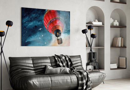 Red hot air balloon floating against starry blue sky displayed as glass wall art above black leather sofa in modern living room.