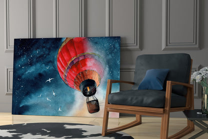 Red hot air balloon floating through a starry blue night sky, displayed as glass wall art beside a wooden chair in a modern interior.
