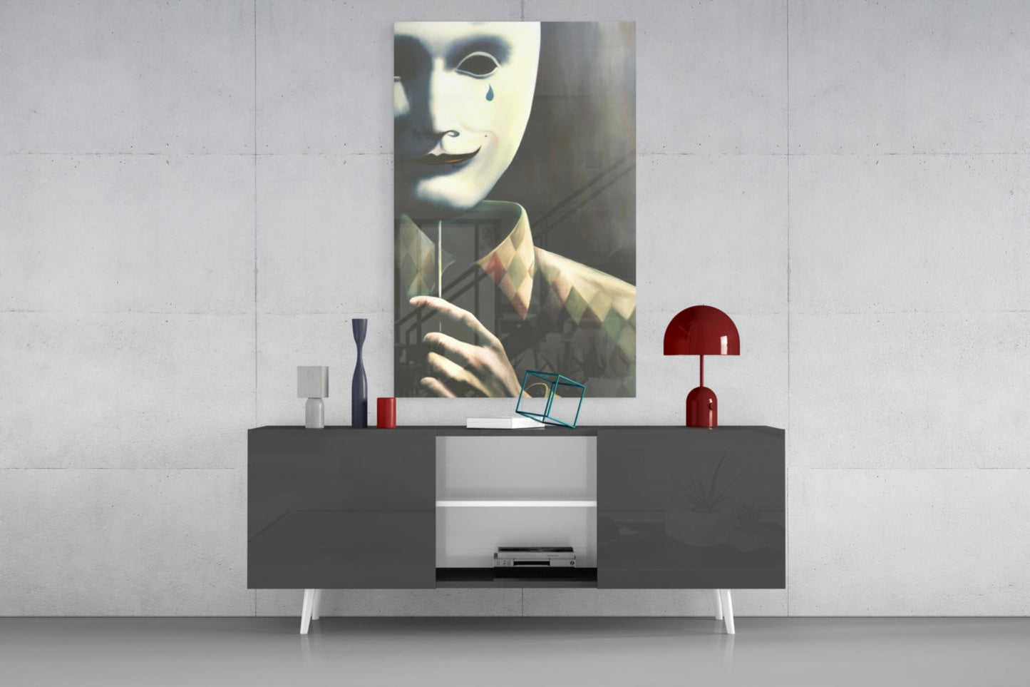 Glass wall art depicting a masked face with teardrop detail displayed above a dark console table with decorative items.