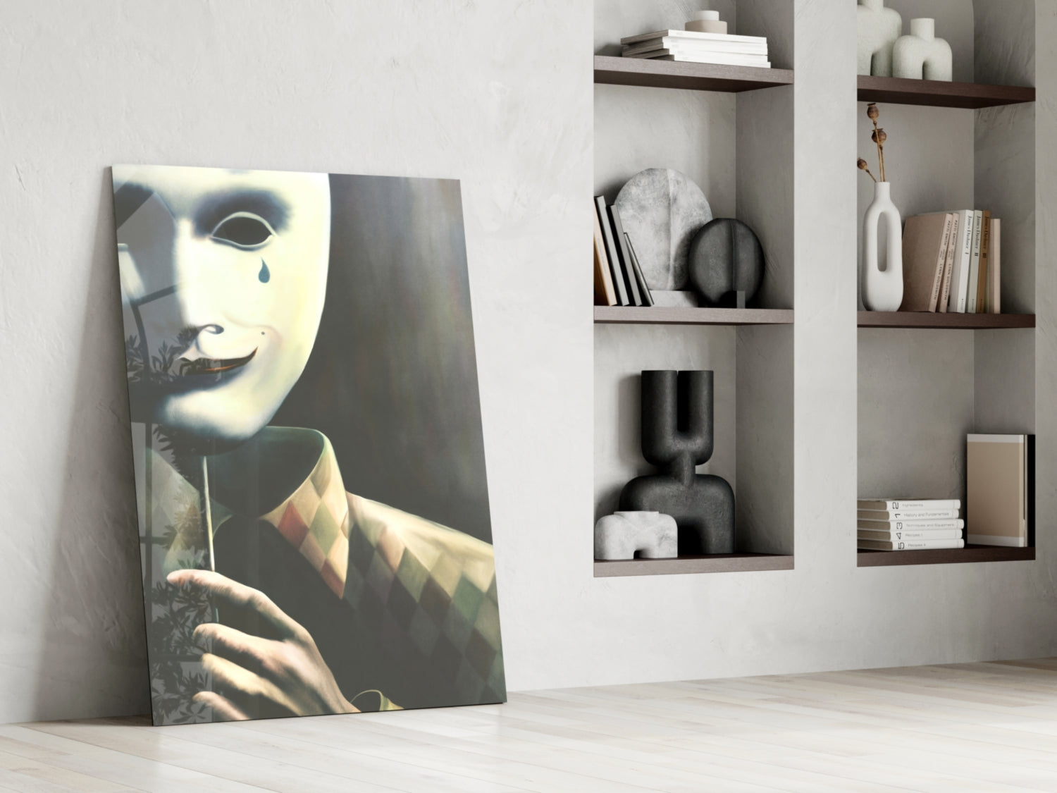 Glass art leaning against white wall displaying pale mask with tear, beside built-in shelving with decorative objects and books.