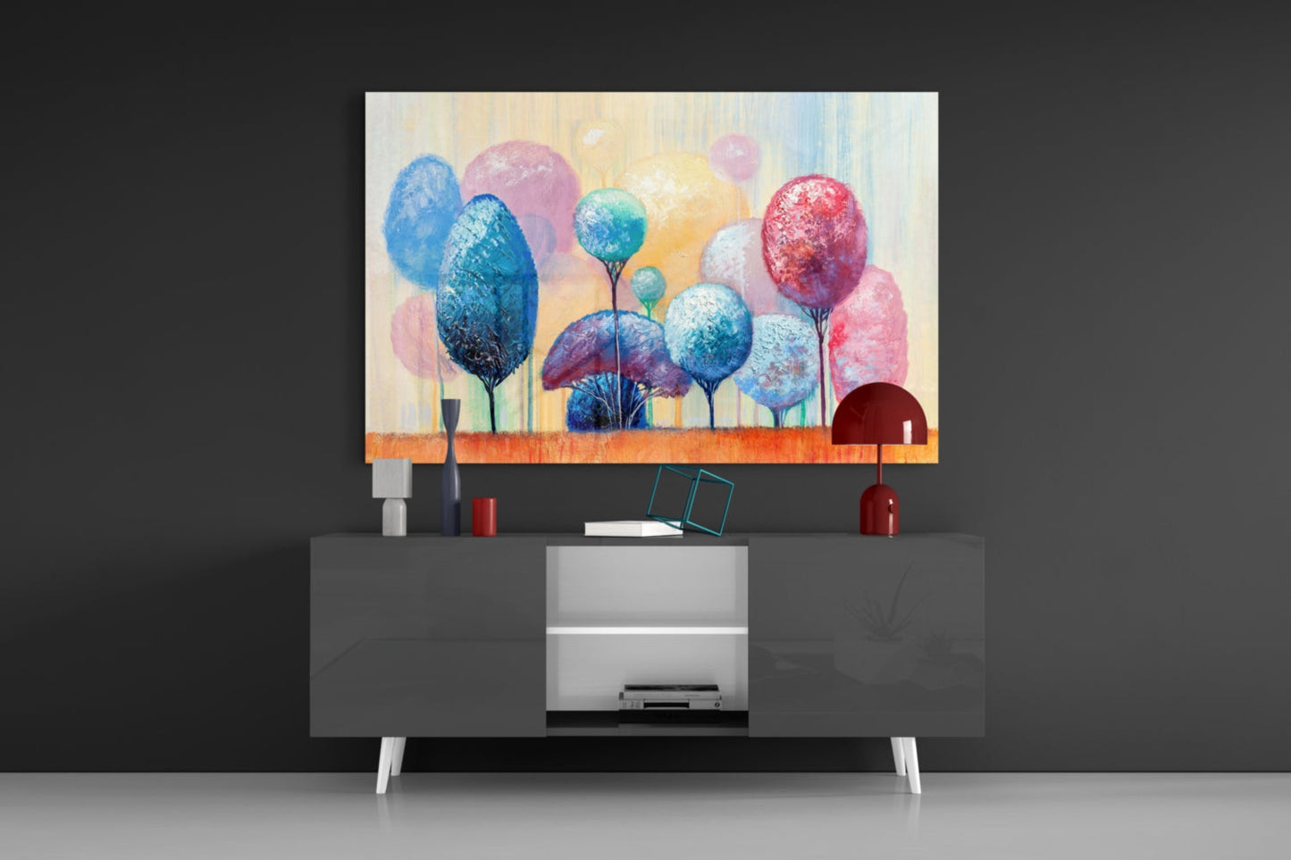 Colorful glass wall art featuring stylized trees in blue, pink, and red tones displayed above a modern dark media console in a minimalist interior setting.