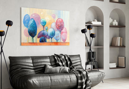 Colorful glass wall art depicting blue, pink, and yellow trees displayed above a black leather sofa in a modern living room.